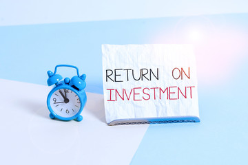 Conceptual hand writing showing Return On Investment. Concept meaning Ratio between the Net Profit and Cost invested Alarm clock beside a Paper sheet placed on pastel backdrop
