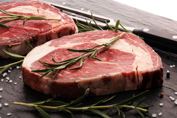 Raw fresh meat Ribeye Steak, seasoning and meat fork on rustic background