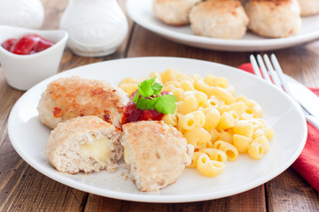 Homemade turkey cutlets with cheese filling on a white plate on a wooden table, horizontal