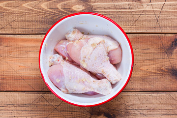 Raw chicken drumsticks in a bowl in a garlic marinade wooden table, top view, selective focus