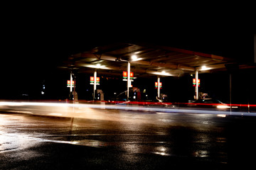 Gas station at night with lights from passing cars as people fill up with petrol