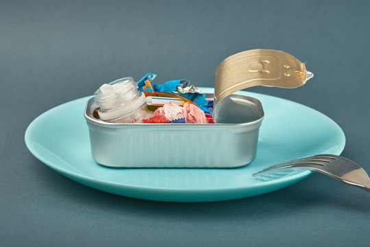 Open tin can on plate and fork. Plastic waste instead of fish inside. Ocean plastic pollution concept
