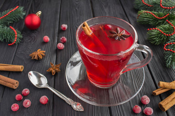 Hot cranberry drink with spices in the glass cup and christmas composition on the black wooden...