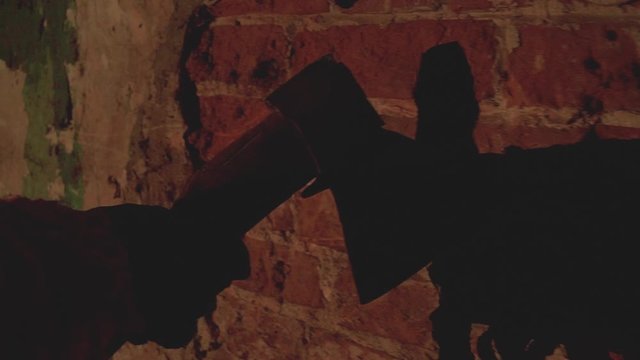 scary hand holding an ax holds an ax along an old destroyed brick wall