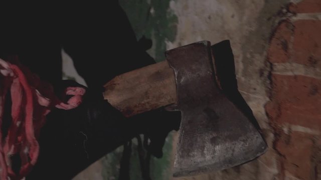 scary hand holding an ax holds an ax along an old destroyed brick wall
