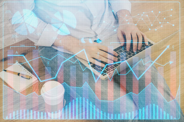 Double exposure of man's hands writing notes with laptop of stock market with forex graph background. Top View. Concept of research and trading.