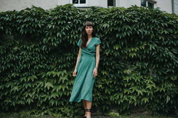 woman wearing an elegant green dress is standing in front of hedge