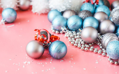 taupe and blue Christmas balls with red ribbon among shiny christmas decorations on pink background
