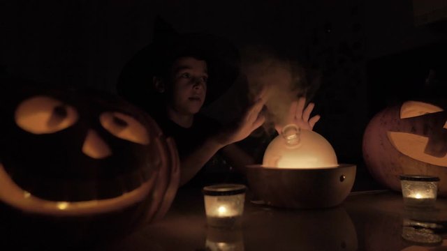 9 year old boy plays wizard on Halloween. With a magic lamp and a pumpkin on the table at night.