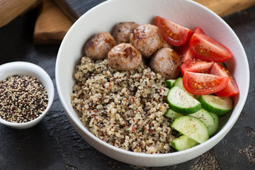 Closeup of a white bowl with quinoa, roasted meatballs and fresh vegetables, studio shot