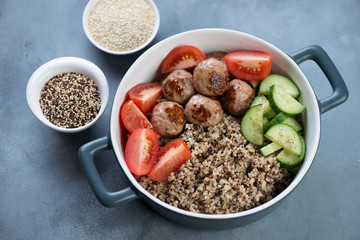 Food bowl with quinoa, roasted meatballs, fresh tomatoes and cucumber, elevated view over grey concrete background