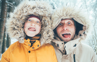 Father and son fooling into the camera. They showing their tongues and making grimaces. Parent and children winter holidays spending concept image.
