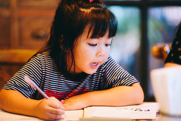 Little asian girl at home doing homework.4 years old girl writing in notebook.