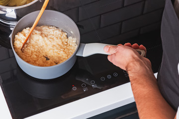 Man's hands close-up stirring risotto in a pot with wooden spatula.