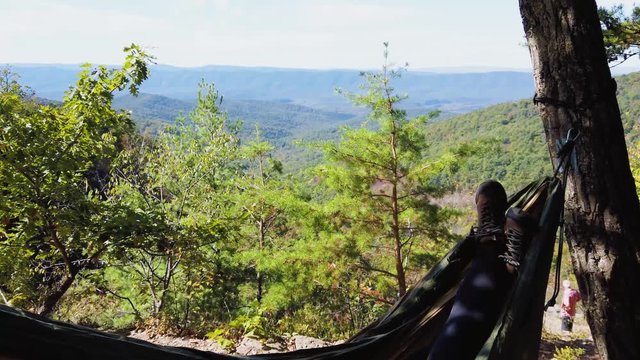A hiker with hiking boots, relaxing and swinging on the hammock amidst dense green jungle on a bright sunny day. Slow motion.Concept of leisure, adventure and rejuvenation.
