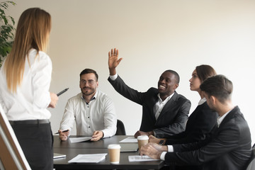 Motivated biracial male employee raise hand answering at team training