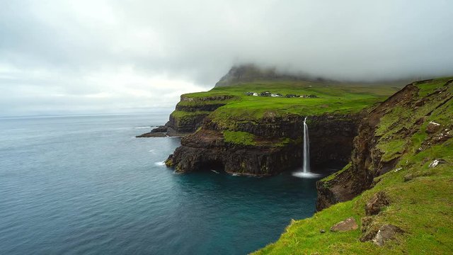 Scenic view of popular Mulafossur Waterfall with the village Gasadalur in background, Faroe Islands.
