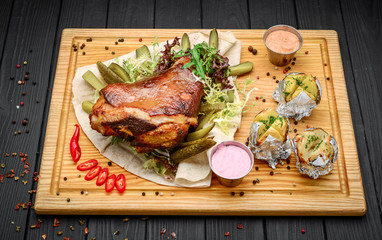 Baked Eisbein with wegetables on wooden board.