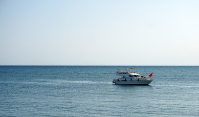 Fototapeta premium White motor boat with a red flag on the background of the sea and horizon. A wonderful trip by sea on a yacht. Unforgettable summer vacation at sea.