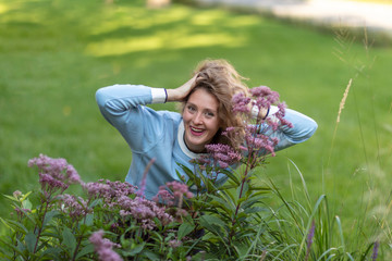 Girl on the green lawn. Smile, flowers on a background of a city park.