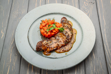 grilled meat with sauce and stewed vegetables on a wooden table