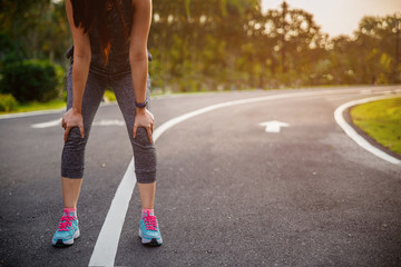 Female runner athlete knee injury and pain. Woman suffering from painful knee while running in the park.