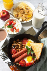 Keto breakfast: fried eggs, sausages, beans, bacon, mushrooms, grilled toasts, orange juice, cottage cheese, pancakes and cocoa on a light stone table with copy space.
