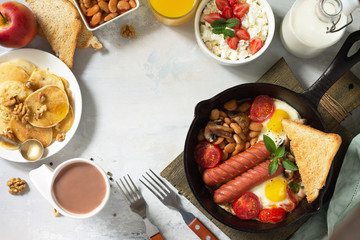 Keto breakfast: fried eggs, sausages, beans, bacon, mushrooms, grilled toasts, orange juice, cottage cheese, pancakes and cocoa on a light stone table. Top view flat lay background with copy space.