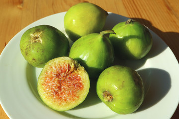 Plate of green whole fresh figs with a cross section fig on wooden table