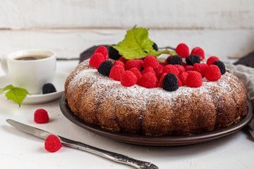 Christmas, holiday cake sprinkled with powdered sugar. Top of raspberry and blackberry. Nearby is a cup of hot coffee. On white background. Copy space. 
