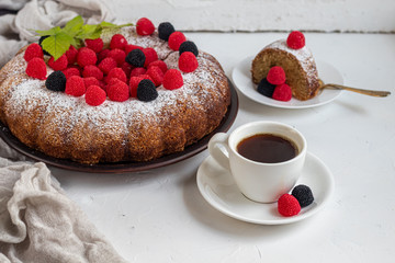 Christmas, holiday cake sprinkled with powdered sugar. Top of raspberry and blackberry. Nearby is a cup of hot coffee. On white background. Copy space. 