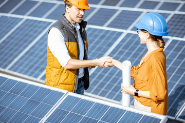 Two successful engineers or architects having a deal, shaking hands while standing between rows of solar panels on a photovoltaic power plant