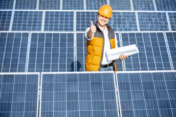 Portrait of a handsome engineer in protective helmet standing with blueprints on a solar power...