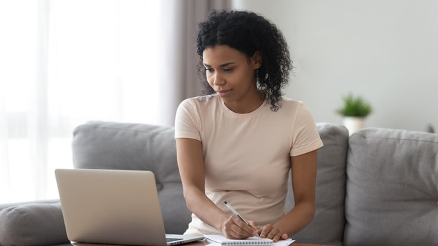 Focused African American Woman Using Laptop, Making Notes