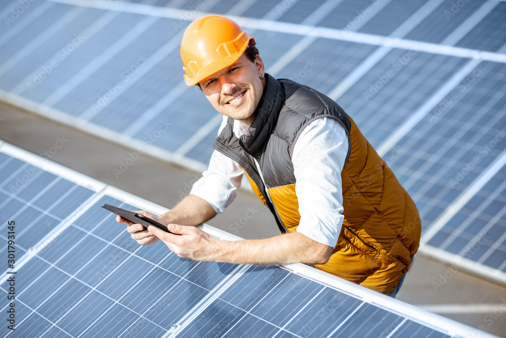 Wall mural portrait of a happy engineer in protective helmet standing with digital tablet on a solar power plan
