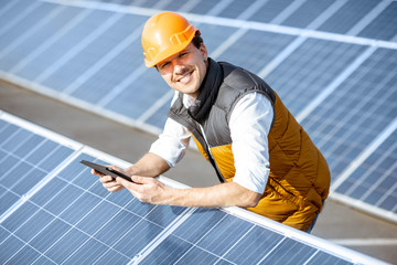 Portrait of a happy engineer in protective helmet standing with digital tablet on a solar power...