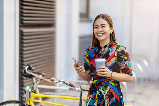 Young hipster woman with her bike and smartphone, drinking coffee