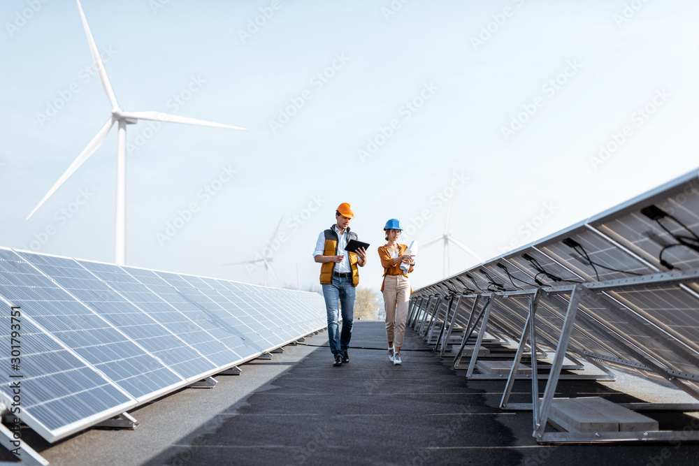 Wall mural view on the rooftop solar power plant with two engineers walking and examining photovoltaic panels. 