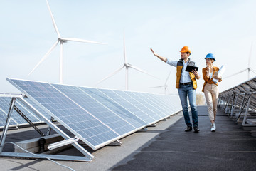 View on the rooftop solar power plant with two engineers walking and examining photovoltaic panels....