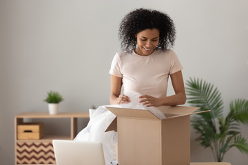 Smiling African American woman unpacking parcel, removing bubble wrap