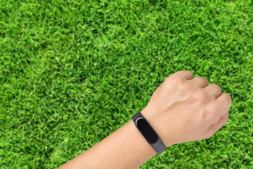 Hand with fitness or activity tracker on green grass background