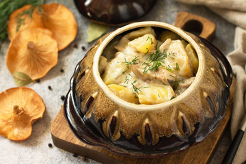 Red mushrooms with stewed potatoes close-up, with sour cream and spices in a ceramic pot on a stone countertop.