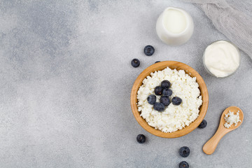 Cottage cheese , farmers cheese in wooden bowl, wooden spoon , milk, sour cream and textile on blue background.