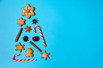 Christmas composition. Christmas tree is made of gingerbread snowflakes and men, caramel canes, spices and red bells on a light blue background. Christmas, winter, New year.