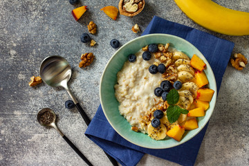 Healthy food for Breakfast, vegetarian and diet food concept. Oatmeal porridge with chia, banana, blueberry, fruits and nuts on a stone countertop. Top view flat lay.