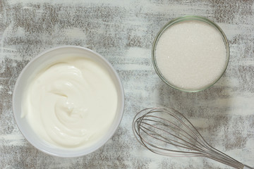 Sour cream in white bowl, whisk and sugar in glass bowl on white background before making cream