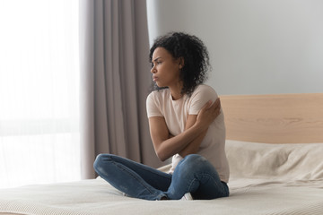 Upset sad African American woman sitting in bed alone