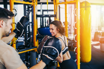 Obraz premium Young attractive woman with instructor on kickboxing training. She hitting or punching in big yellow boxing bag.