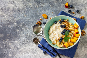 Healthy food for Breakfast, vegetarian and diet food concept. Oatmeal porridge with chia, banana, blueberry, fruits and nuts on a stone countertop with copy space.