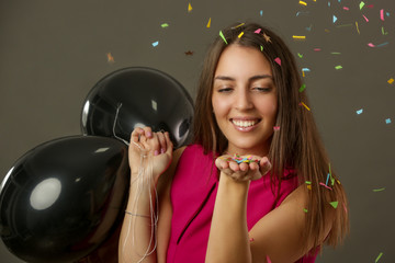 Attractive woman holding black baloons and dancing under falling confetti, party and holiday season...